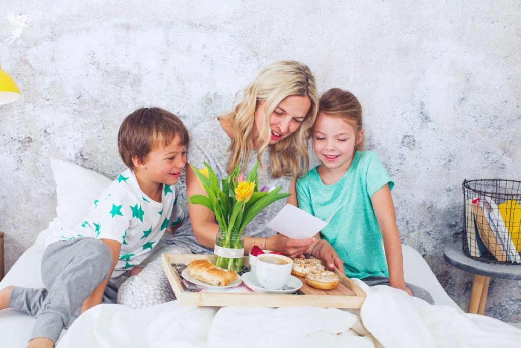 mom with children in bed opening card with daffodils and a breakfast tray mothers day experience at home