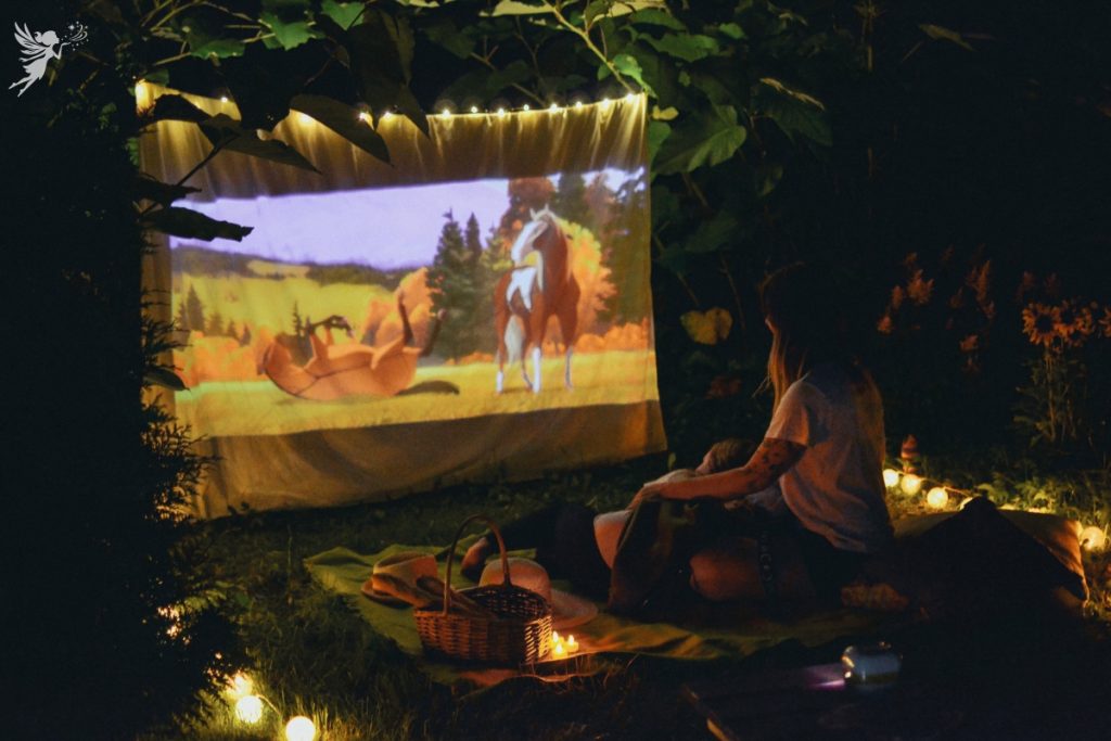 child watching a pony movie on a white sheet tied up in the trees