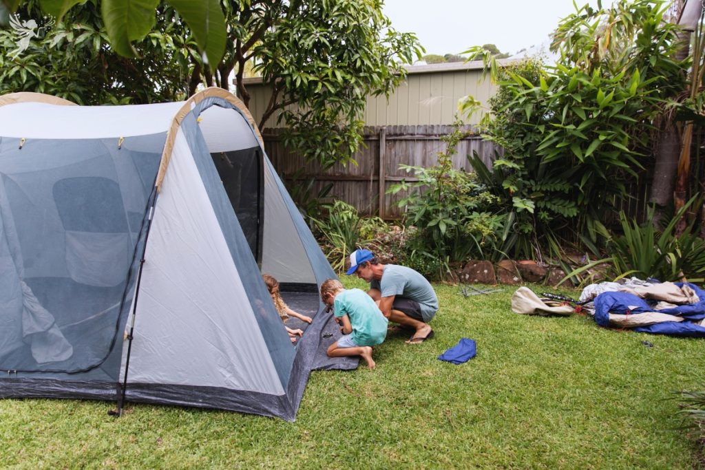 father and children working to set up a tent in a backyard 