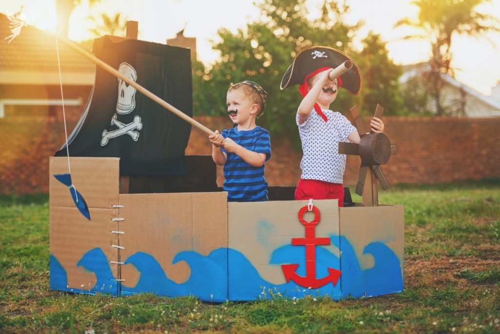 two boys in pirae dress up in a cardboard painted like a pirate ship in the backyard