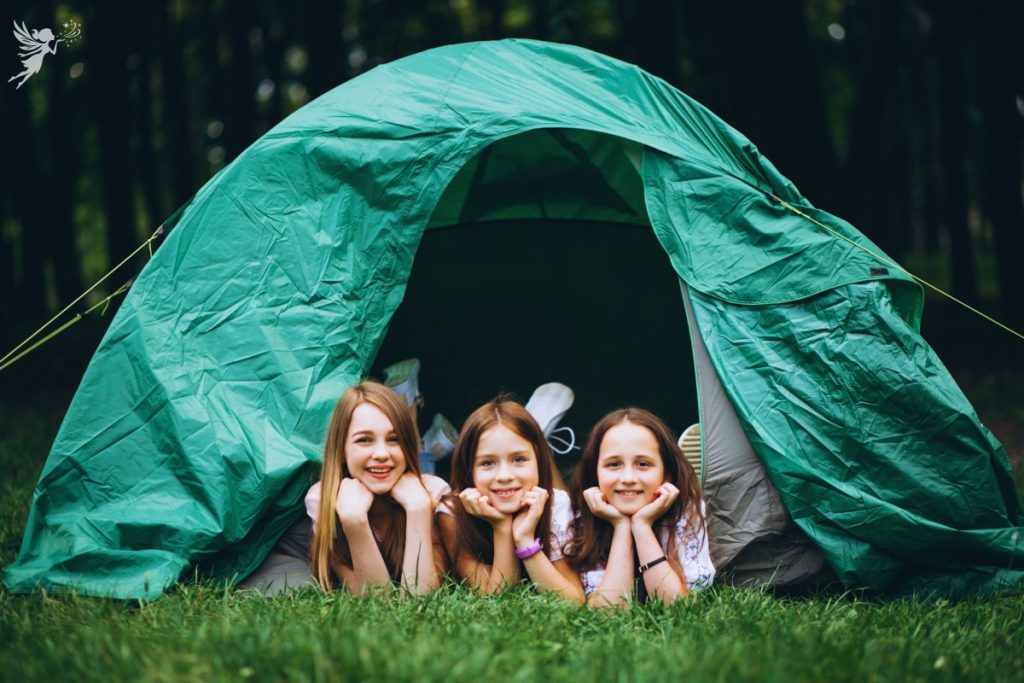 thrill tween girls lying with heads poking out a green tent in the backyard