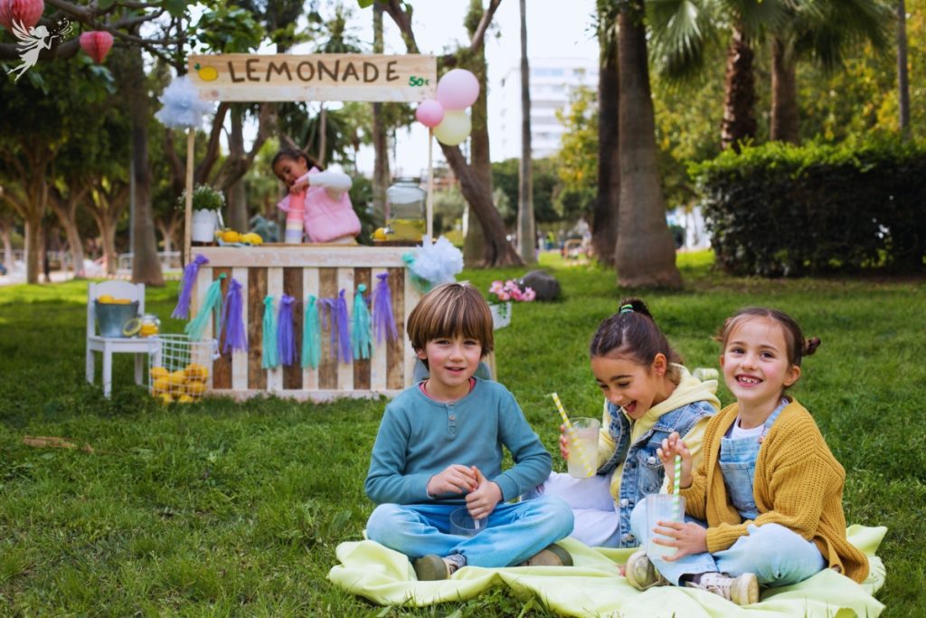 kids having a cute outdoor picnic, in the background a kids lemonade stand
