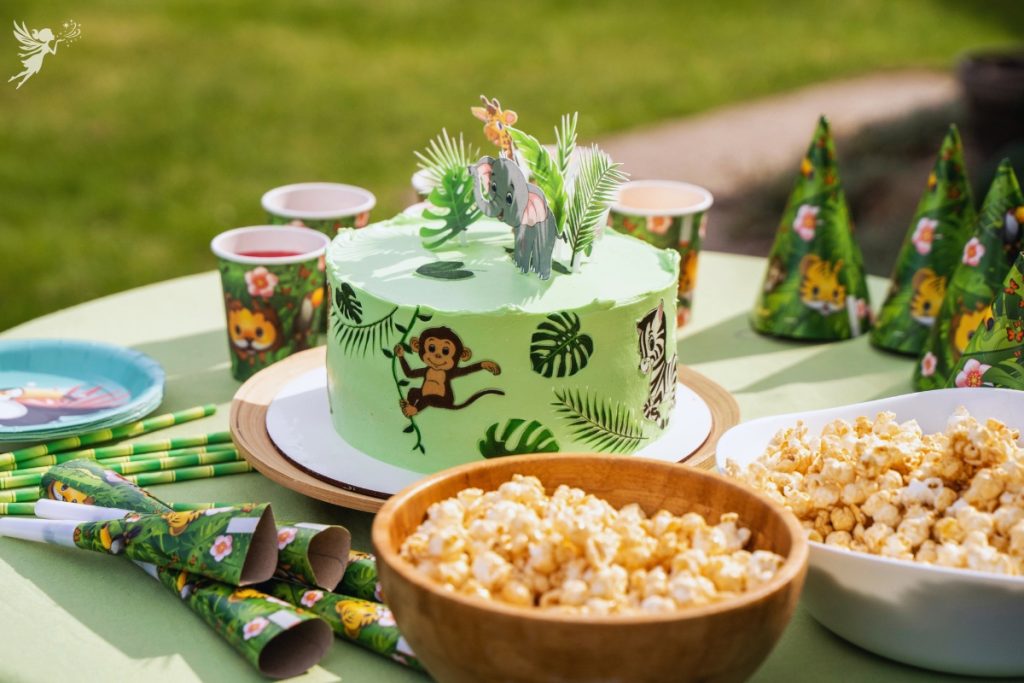 a beautifully decorated safari cake with safari animal cups and plates in an outdoor setting