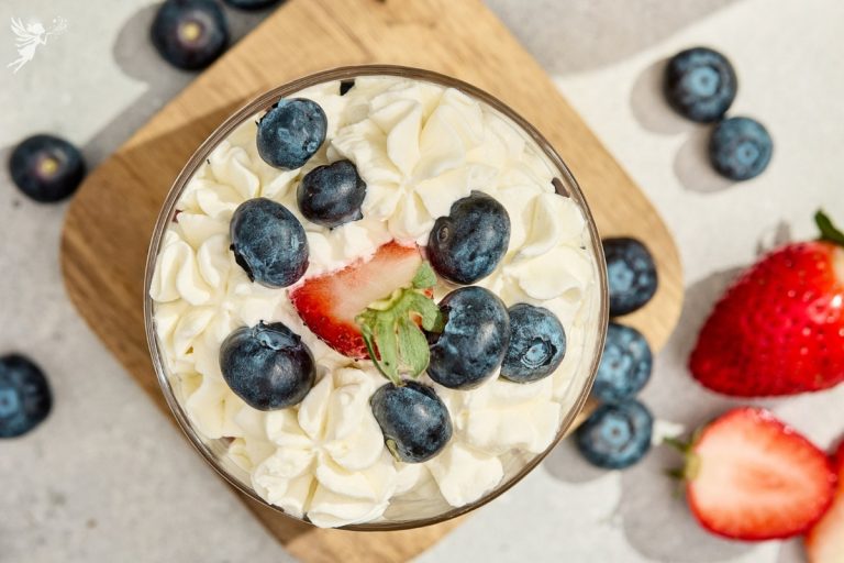 Overhead view of red white and blue berry trifles topped with fresh blueberries, a strawberry slice, and piped whipped cream.