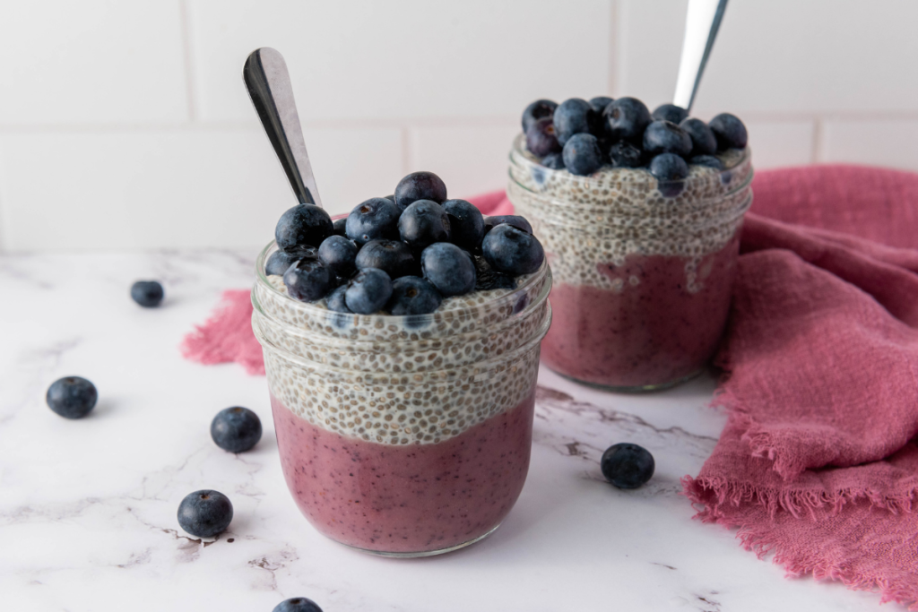 Two glass jars filled with layered Blueberry Chia Pudding Cups topped with a mountain of fresh blueberries and silver spoons.