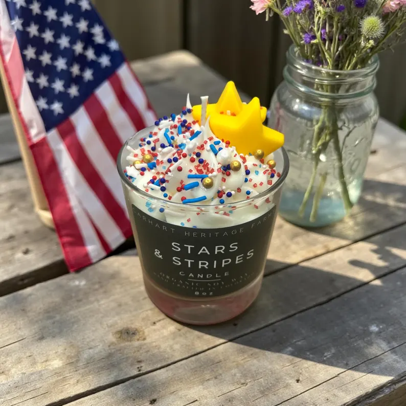A Stars & Stripes soy candle topped with whipped wax and red, white, and blue sprinkles — charming 4th of July hostess gifts displayed beside an American flag. Etsy