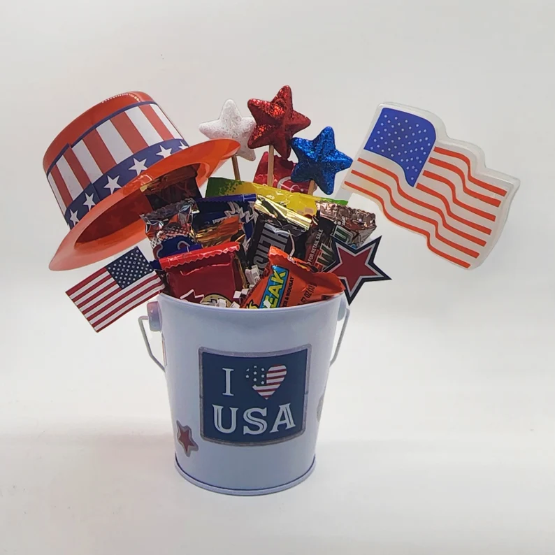 A festive 4th of July hostess gift featuring a patriotic candy basket filled with assorted chocolates, glitter stars, mini American flags, and an Uncle Sam hat. Etsy