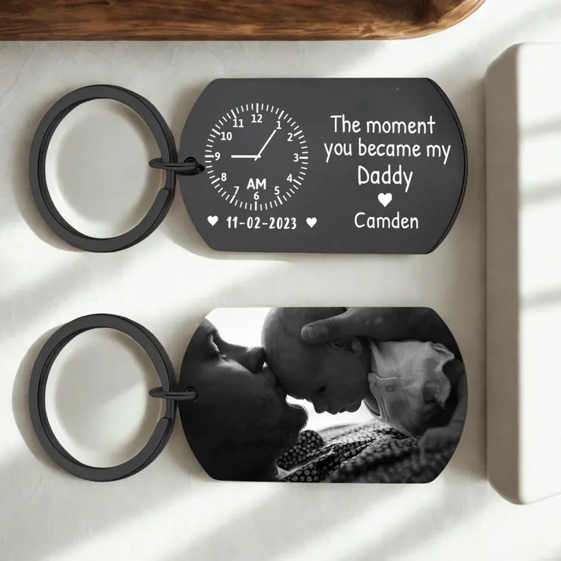 A black metal keychain engraved with a birth time, date, and "The Moment You Became My Daddy," with a photo on the back, a meaningful first Father's Day gift idea. Etsy