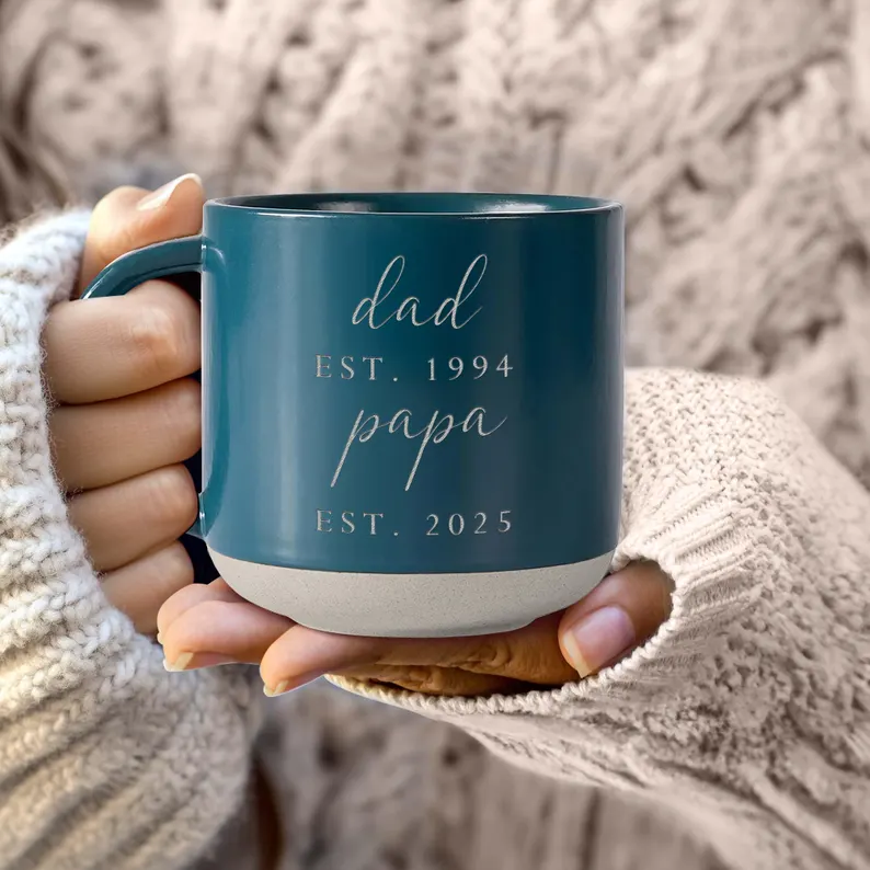 Hands cradling a teal ceramic mug engraved with "Dad Est. 1994 Papa Est. 2025," a thoughtful and elegant first Father's Day gift idea celebrating a new grandpa milestone. Etsy