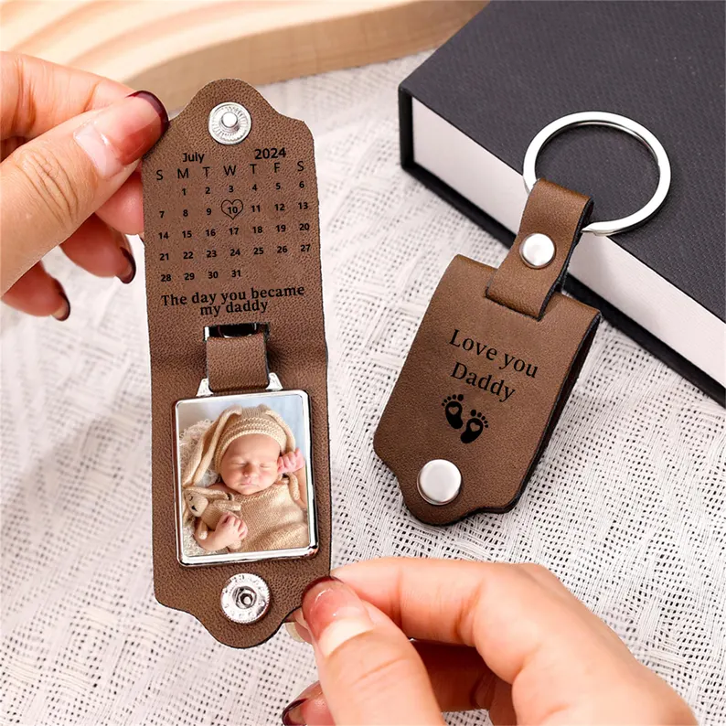 A brown leather keychain unfolding to reveal a baby photo, birth calendar date, and "Love You Daddy" engraving, a sentimental and practical first Father's Day gift idea. Etsy