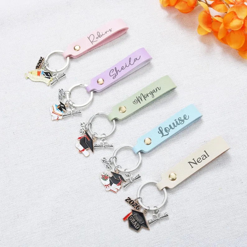 Five pastel leather keychains personalized with different names and graduation cap charms in various colors, making charming and affordable graduation gifts. Etsy