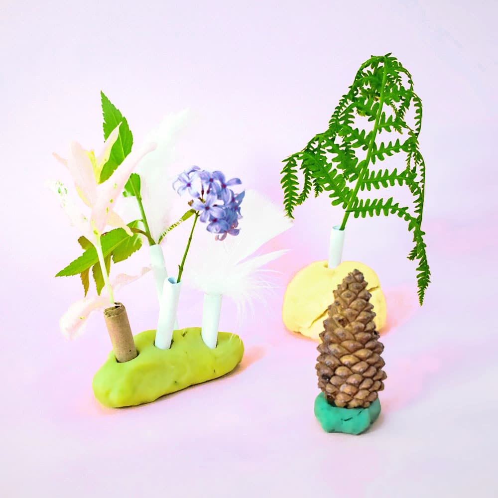 A nature-inspired fairy forest scene built with playdough, paper straws, flowers, and pine cones for fairy party crafts and activities.