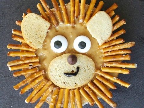 Bagel lion face made with peanut butter and pretzel sticks, a creative safari animal party food idea for kids