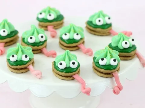 Green chameleon Nutter Butter cookies with candy eyes and pink tongues on a cake stand, adorable safari animal party food ideas