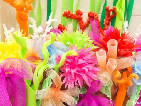 A vibrant DIY coral reef party decoration made from colorful tissue paper, pipe cleaners, ribbon, and foam in bright tropical colors