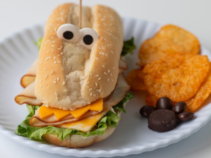 Crocodile-shaped sandwich with googly eyes served with chips, a fun safari animal party food idea for kids