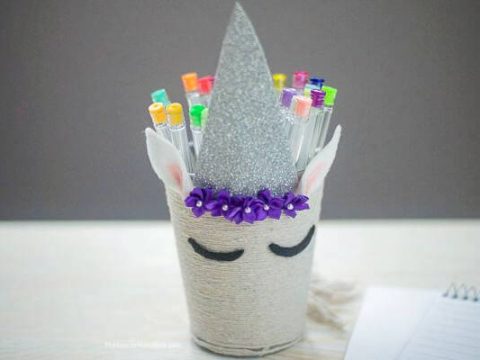 A DIY unicorn pencil holder wrapped in yarn with a glitter horn is a creative unicorn party craft and activity kids will love
