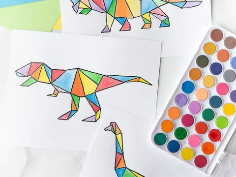Three geometric stained glass style dinosaur coloring pages with a watercolor paint set on a marble surface