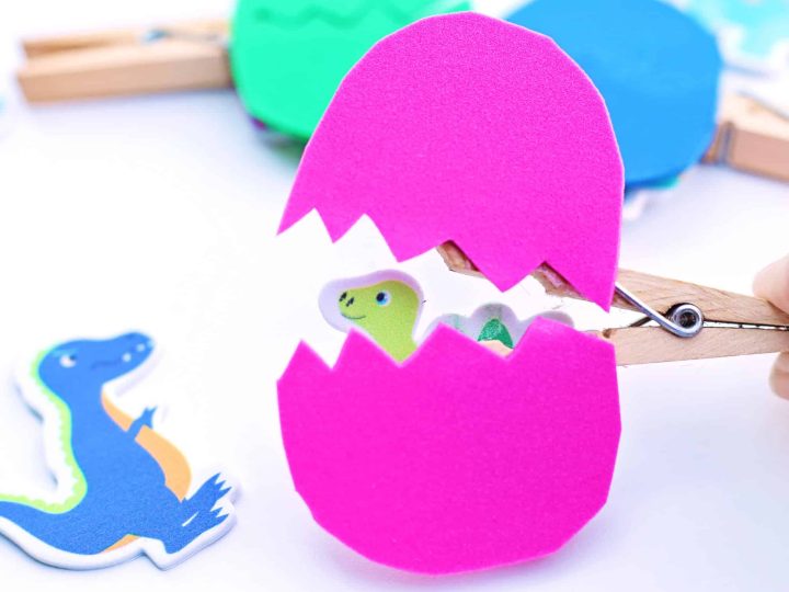Bright pink foam hatching dinosaur egg craft opened with a clothespin revealing a baby dinosaur inside