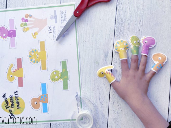 Child's hand wearing five colorful printable paper dinosaur finger puppets beside a cut-out template sheet