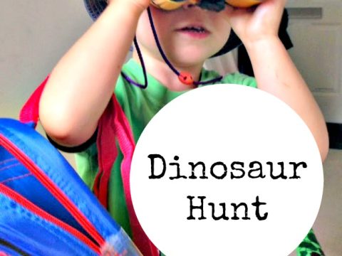 Young child wearing a hat and looking through yellow toy binoculars during an outdoor dinosaur hunt party activity
