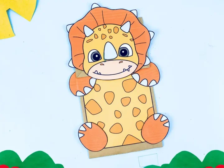Completed orange and yellow triceratops dinosaur paper bag puppet craft on a light blue background
