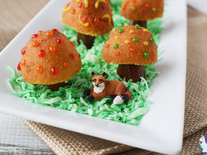 Donut hole toadstools with candy dot spots displayed on green coconut grass with a toy fox — a whimsical and creative fairy party food idea for kids.