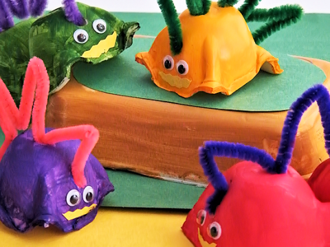 Colorful painted egg carton dinosaurs with googly eyes and pipe cleaner spikes in purple, green, orange, and red