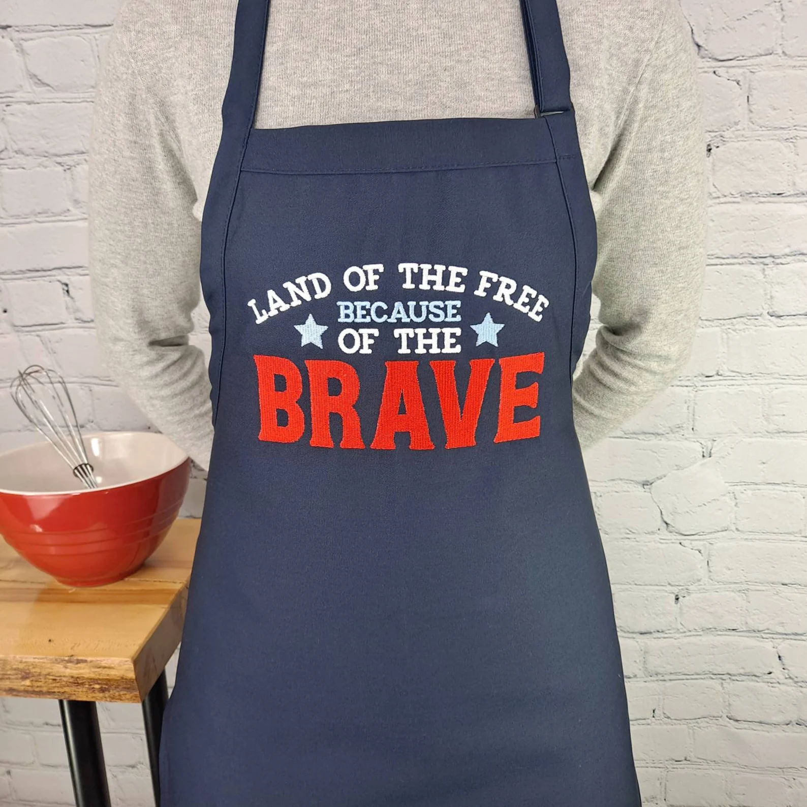 Navy blue embroidered patriotic apron reading 'Land of the Free Because of the Brave' โ a thoughtful 4th of July hostess gift idea.