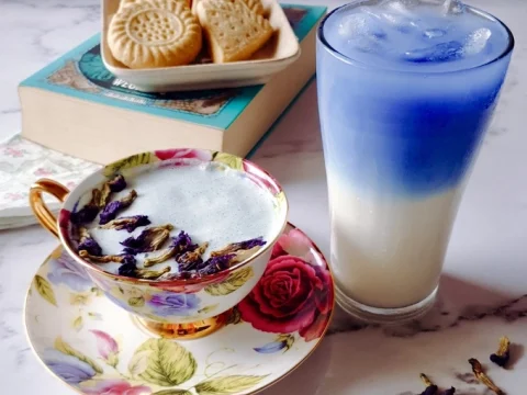 Vibrant blue butterfly pea latte served hot in a floral teacup and iced in a tall glass — an enchanting and Instagram-worthy fairy party food drink idea.