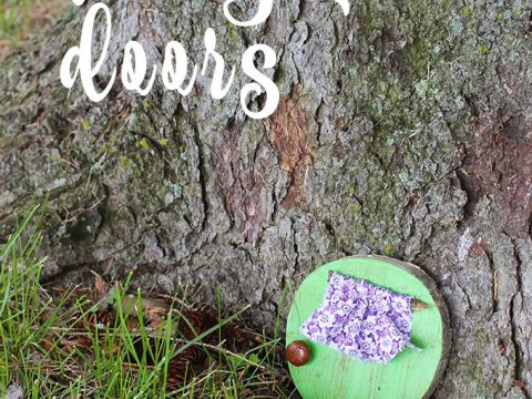 A small green fairy door leaning against a tree trunk in the grass, a whimsical fairy party crafts and activities make-and-take project.