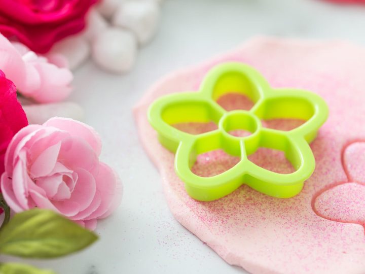 Soft pink glittery fairy dough with a flower-shaped cookie cutter and floral accents, a sensory fairy party crafts and activities idea.