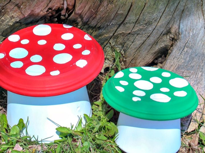 Two painted clay pot toadstools in red and green sitting in the grass, a fun DIY fairy party crafts and activities decoration.