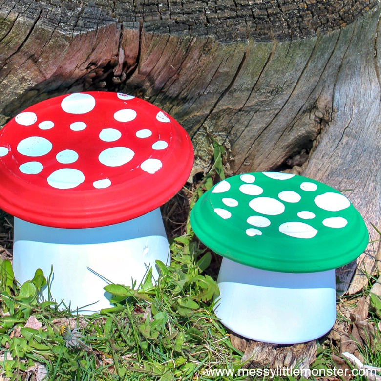 Two painted clay pot toadstools in red and green sitting in the grass, a fun DIY fairy party crafts and activities decoration.