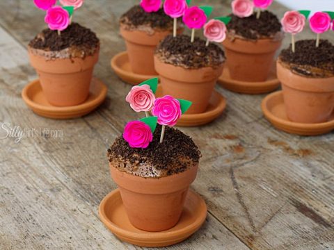 Chocolate cupcakes baked inside terracotta flower pots topped with Oreo crumb dirt and pink paper rose picks — a charming fairy garden fairy party food idea.