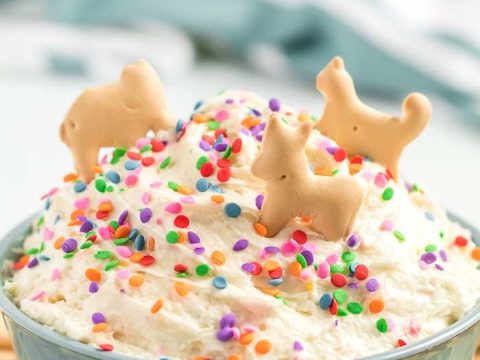 Creamy funfetti dip topped with sprinkles and animal crackers in a blue bowl, a playful safari animal party food idea