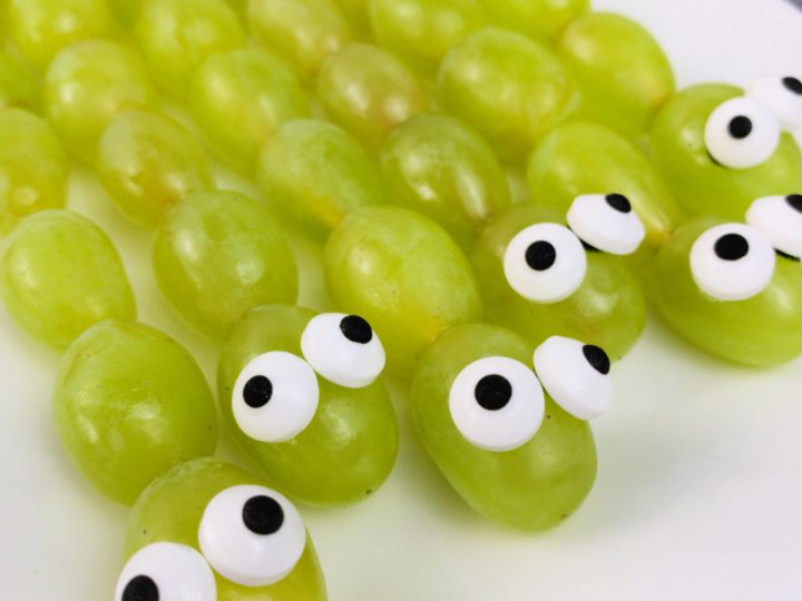 Green grape snakes on skewers with candy eyes lined up on a white platter, simple safari animal party food ideas kids will love