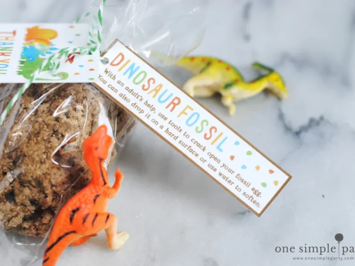 Fossil-style dino egg party favor in a cellophane bag with small plastic dinosaur figurines on a marble surface