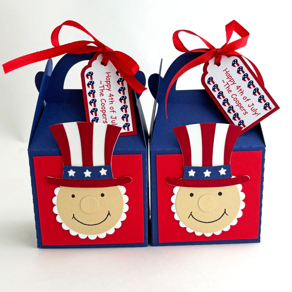 Two navy blue gable boxes with smiling Uncle Sam face decorations and personalized Happy 4th of July gift tags tied with red ribbon, adorable 4th of July party favors.