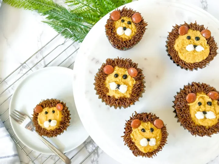 Decorated lion face cupcakes with chocolate frosting manes and candy features on a white cake stand, easy safari animal party food ideas