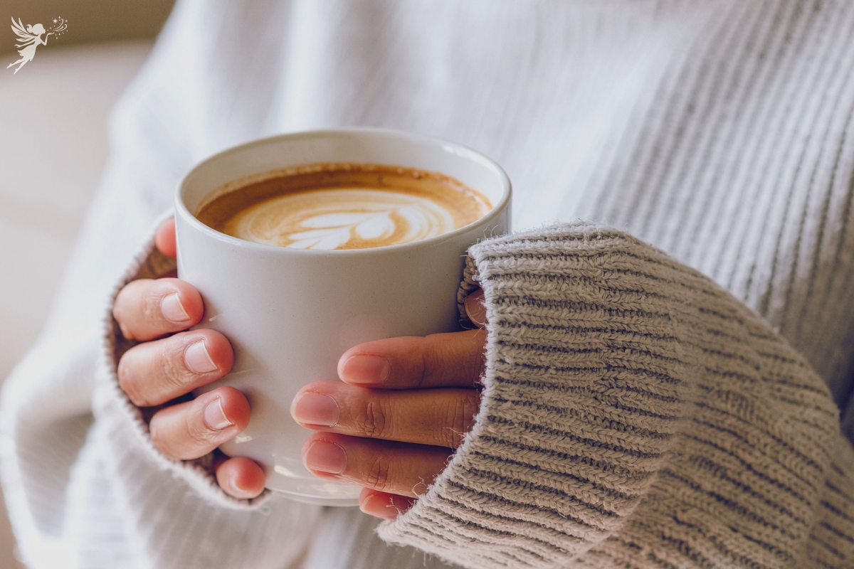 lady in warm woolly jumper cradling a hot latte coffee