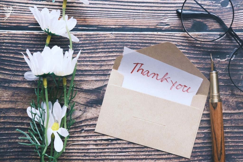 Thank you note sticking out of an envelope with some daisies