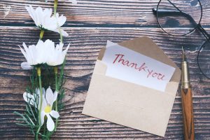 Thank you note sticking out of an envelope with some daisies