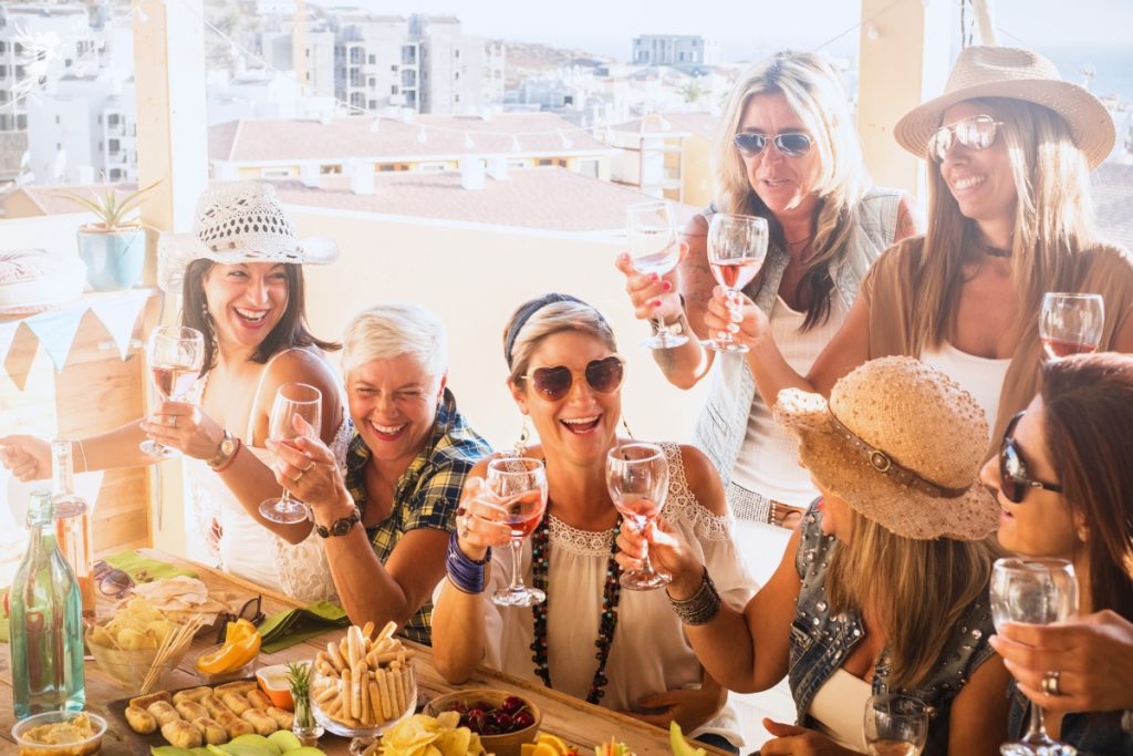 group of older female friends in a sunny holiday location brunch cheers with rose wine