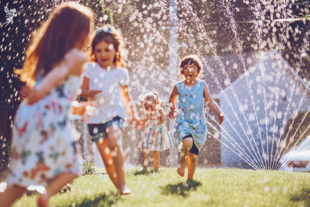 children running through a garden sprinkler