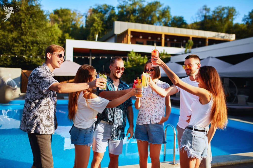 adults in summerwear next to a pool toasting