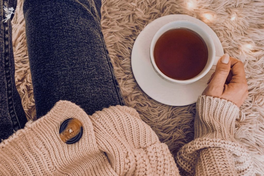 overhead view of a lady sitting on a woolly jug with warm jumper and jeans holding a cup of tea on white cup and saucer