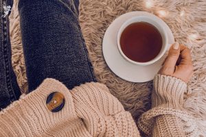 overhead view of a lady sitting on a woolly jug with warm jumper and jeans holding a cup of tea on white cup and saucer