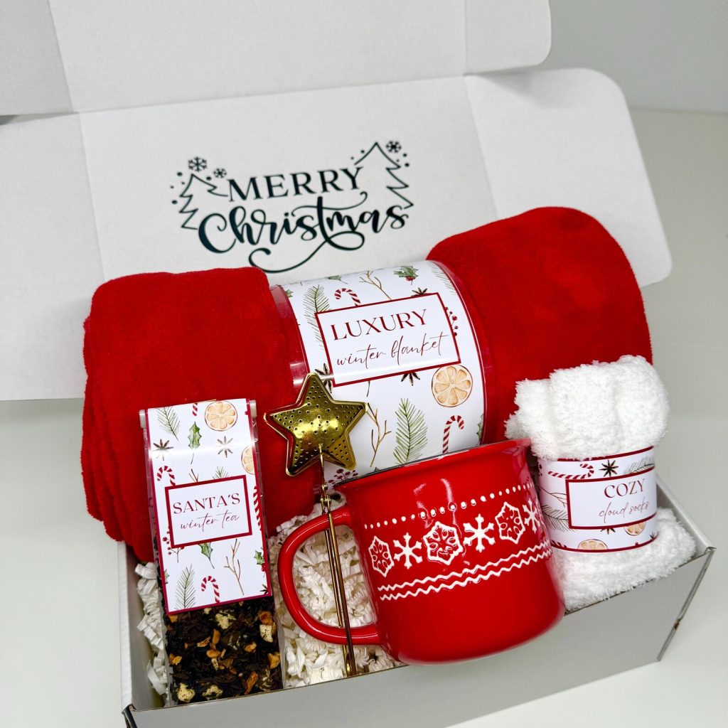 Luxury Christmas gift box with a red snowflake mug, Santa's winter tea, cozy cloud socks, and a plush blanket โ a perfect Christmas hostess gift set.