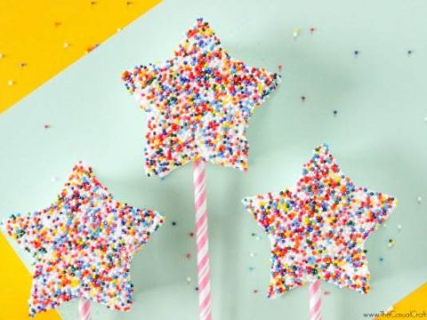 White chocolate star-shaped marshmallow wands covered in rainbow sprinkles on pink striped sticks — a magical and easy fairy party food treat for little guests.
